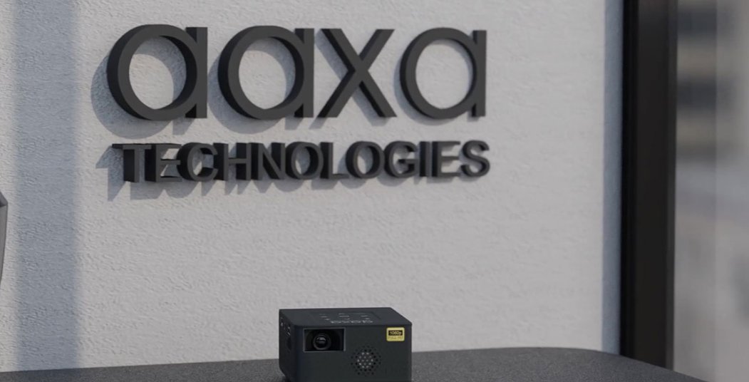 An AAXA pico projector on a counter in front of the AAXA Technologies brand wall